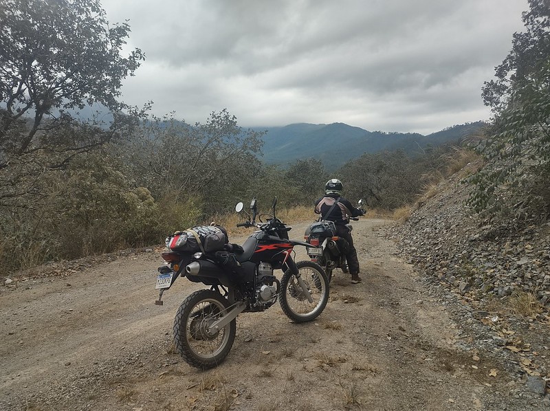 two motorcycles pause on a
        steep gravel road