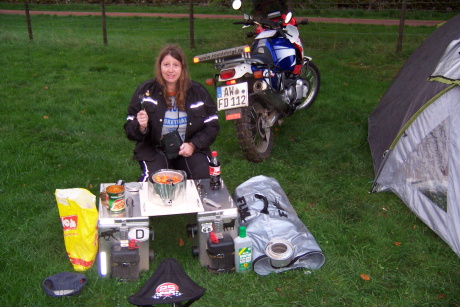Woman at a campsite in a
        field with panniers as chair and table