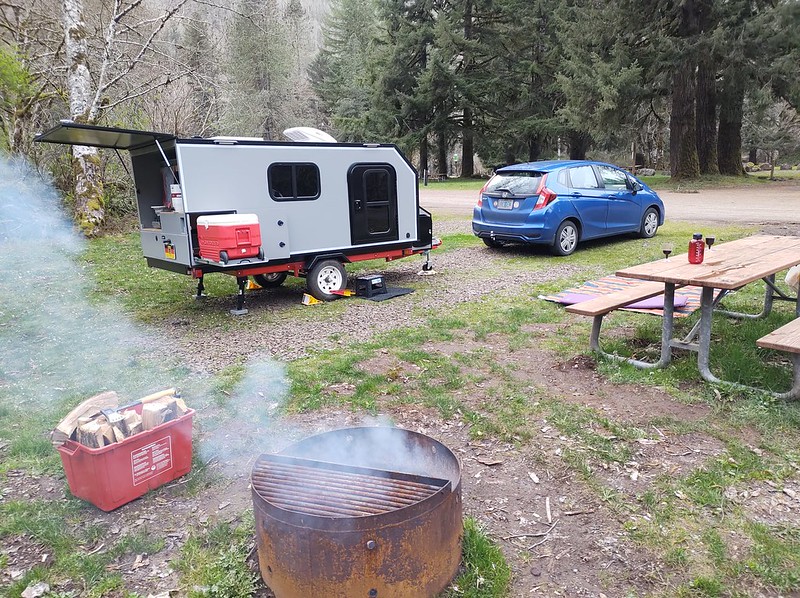 a small, square camper at a campsite next to a picnic table and campfire