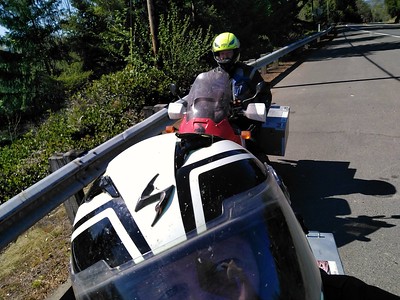 Selfie photo
        taken by a person wearing her motorcycle helmet also showing
        person behind her on a motorcycle and wearing a helmet