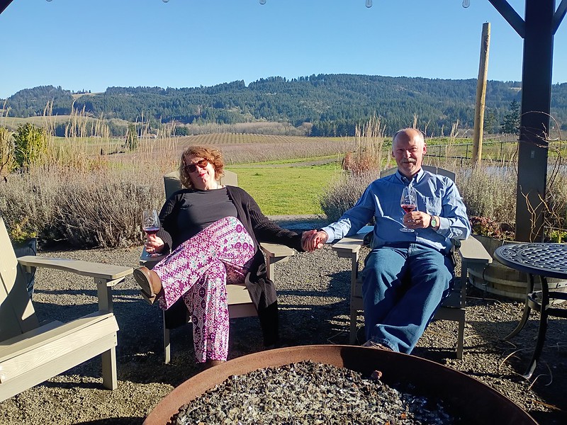 a couple sit outside at a fire pit, with a gorgeous
            view behind then