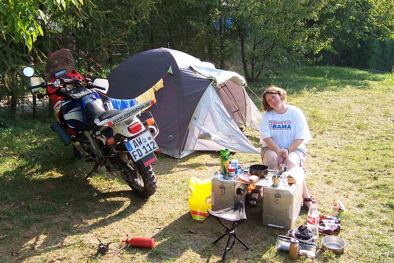 a woman
sits at a pannier table and chairs at a motorcycle campsite