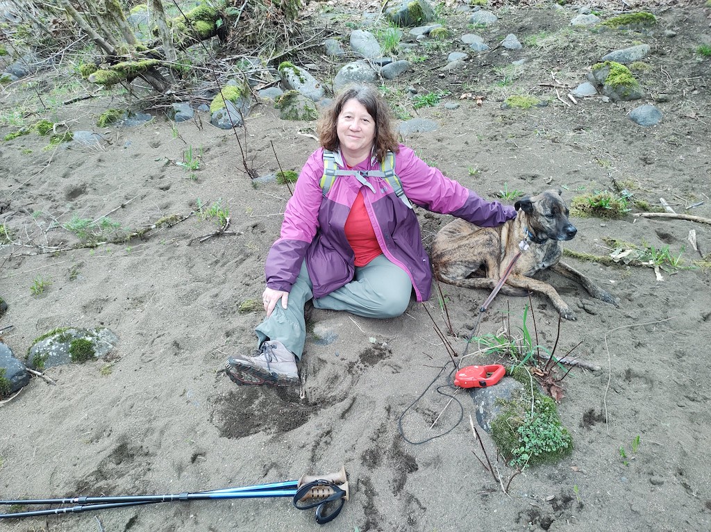 Jayne and Lucinda the dog sitting on a gray, rocky beach, looking up at the camera, very happy